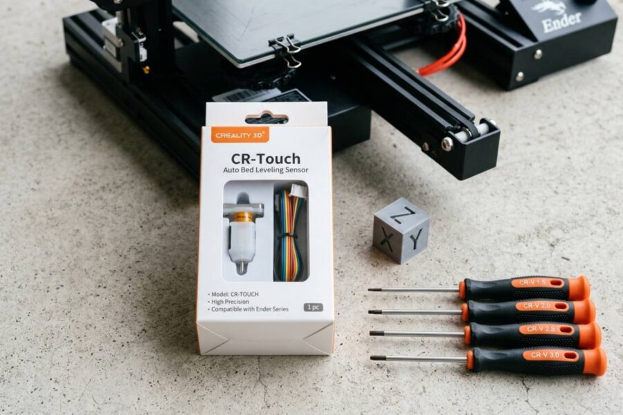 Sensor CR-Touch Creality sobre bancada ao lado de uma Ender 3 para upgrade de nivelamento automático