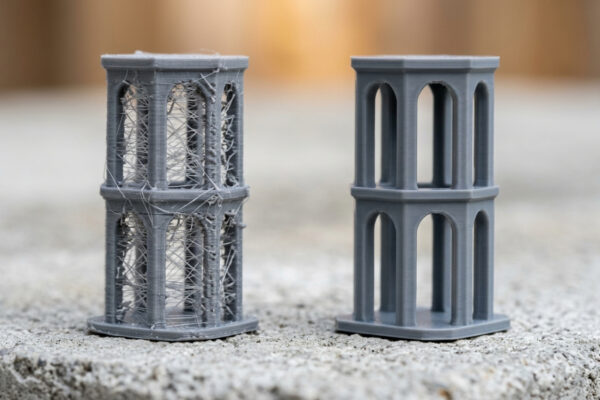 Stringing em peça impressa em 3D com fios de filamento entre paredes, sobre bancada industrial